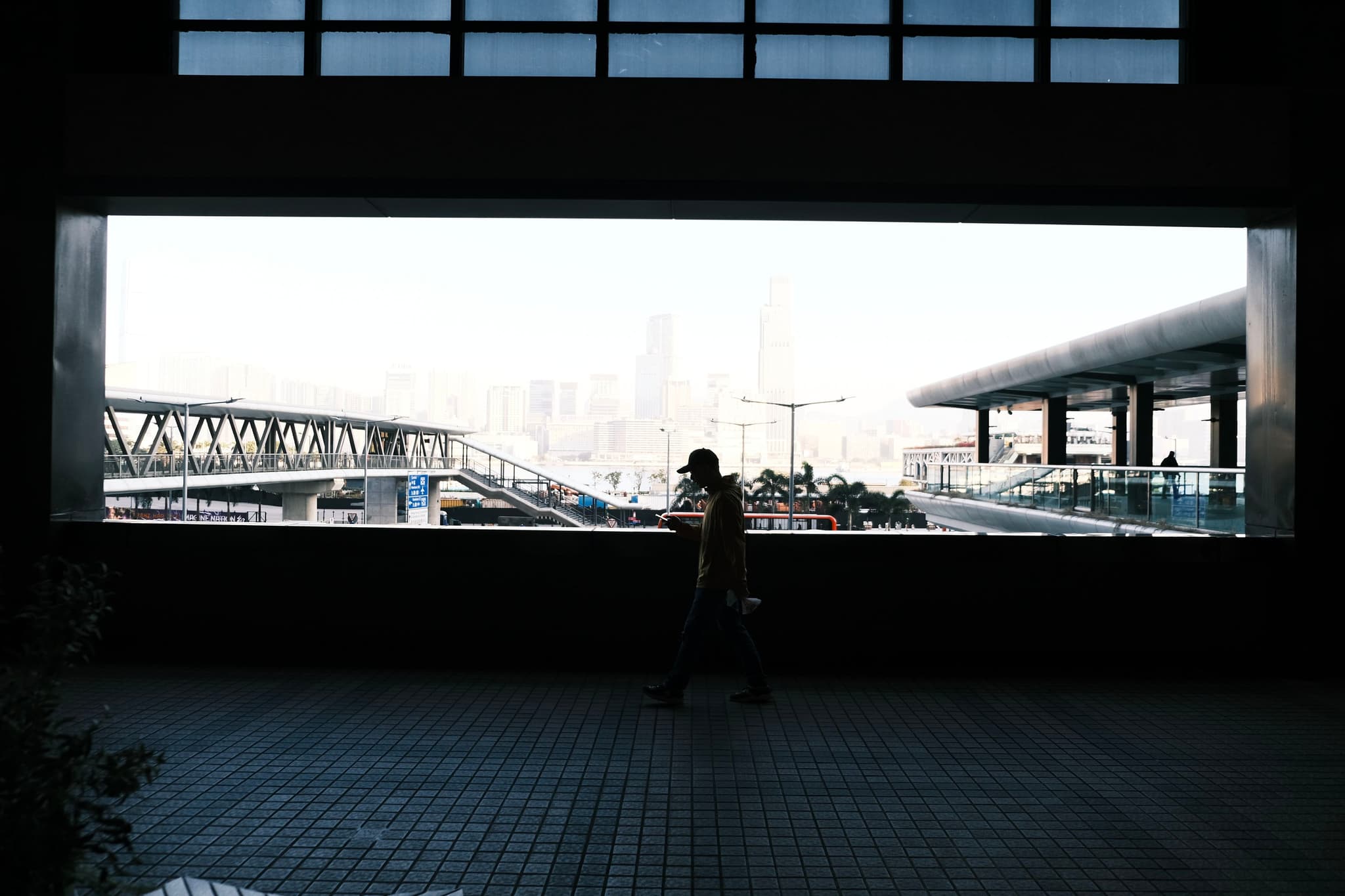 A silhouetted person walking in front of a large window framing an urban cityscape with bridges and modern architecture
