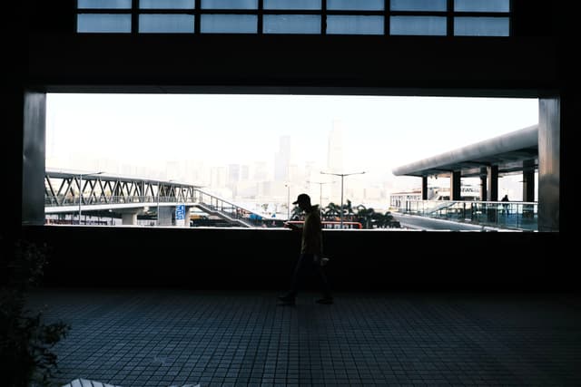 A silhouetted person walking in front of a large window framing an urban cityscape with bridges and modern architecture