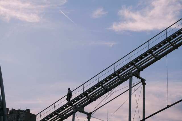 A person walking on an elevated industrial walkway against a backdrop of a blue sky with scattered clouds
