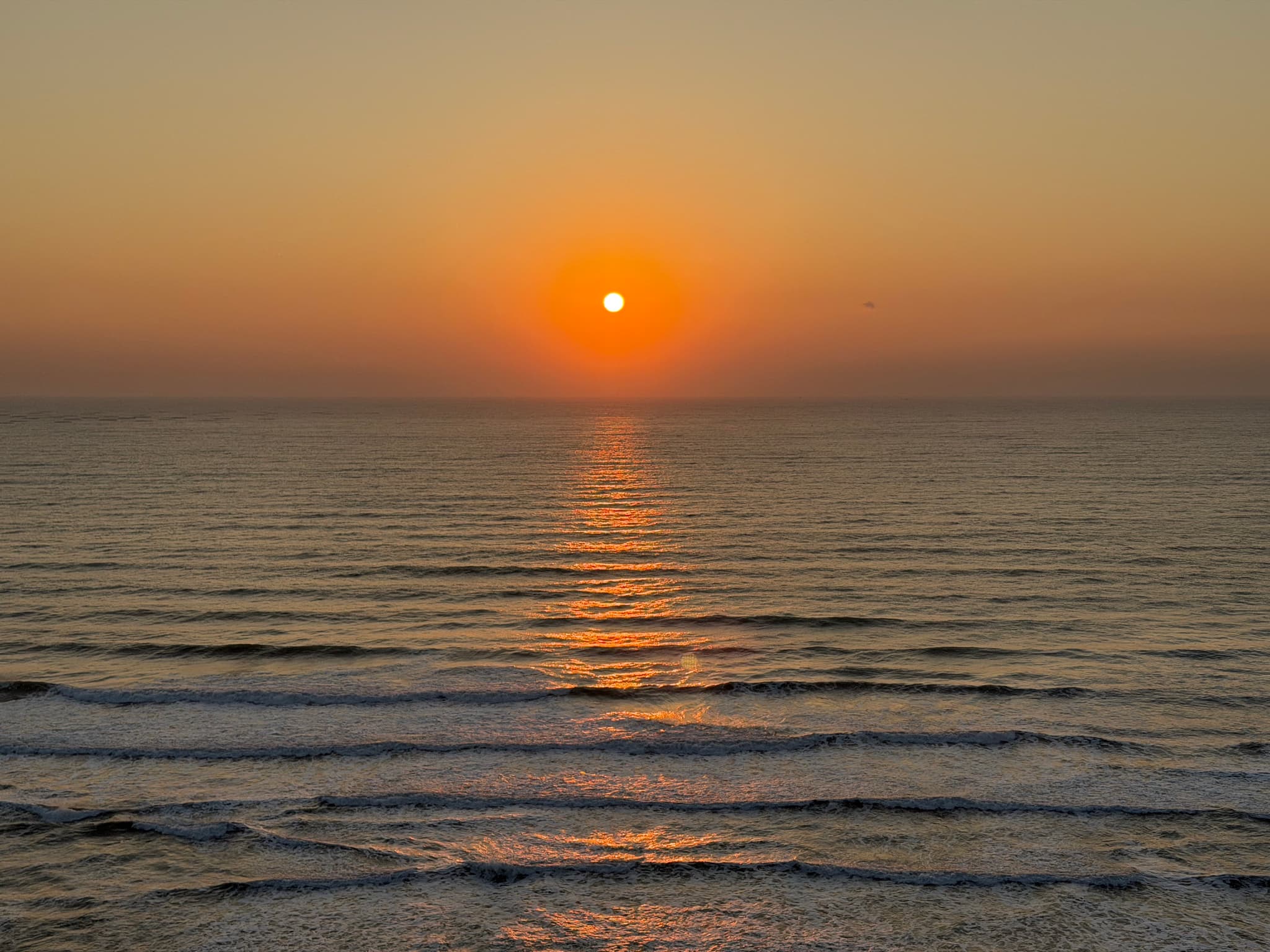A serene sunset over the ocean with gentle waves and a warm orange glow reflecting on the water