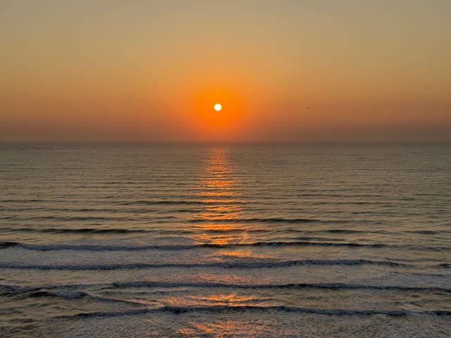 A serene sunset over the ocean with gentle waves and a warm orange glow reflecting on the water