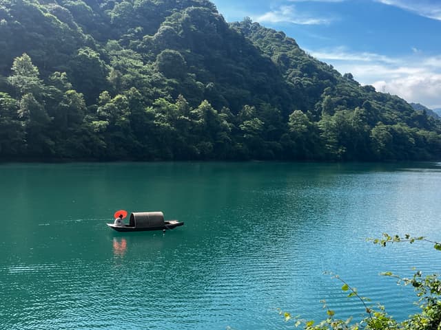 A serene lake surrounded by lush green hills, with a small boat featuring a covered cabin floating on the calm water